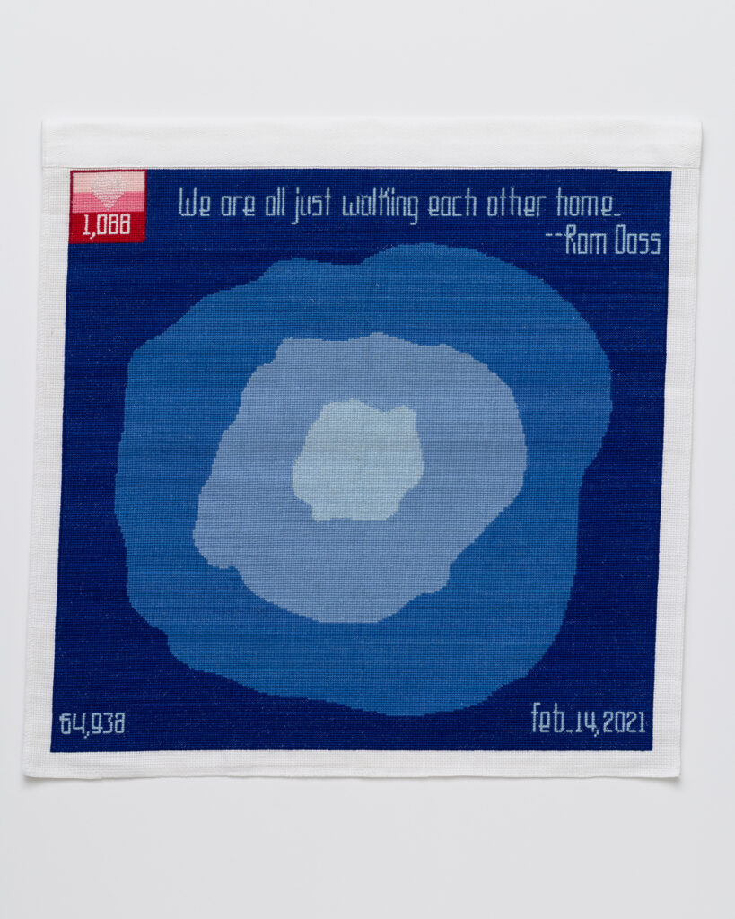 cross stitch embroidery of abstract blue splotches, with lightest blue in middle, two slightly darker, then dark blue background. There is a red square in the top left with three shades of pink with 