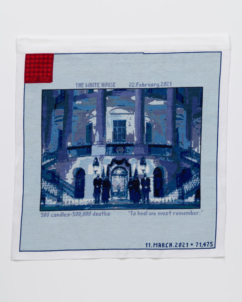 Cross stitch embroidery of picture of President Biden in front of the White House, standing with other figures, stitched in blue threads. There is a solid light blue border around the image, with 