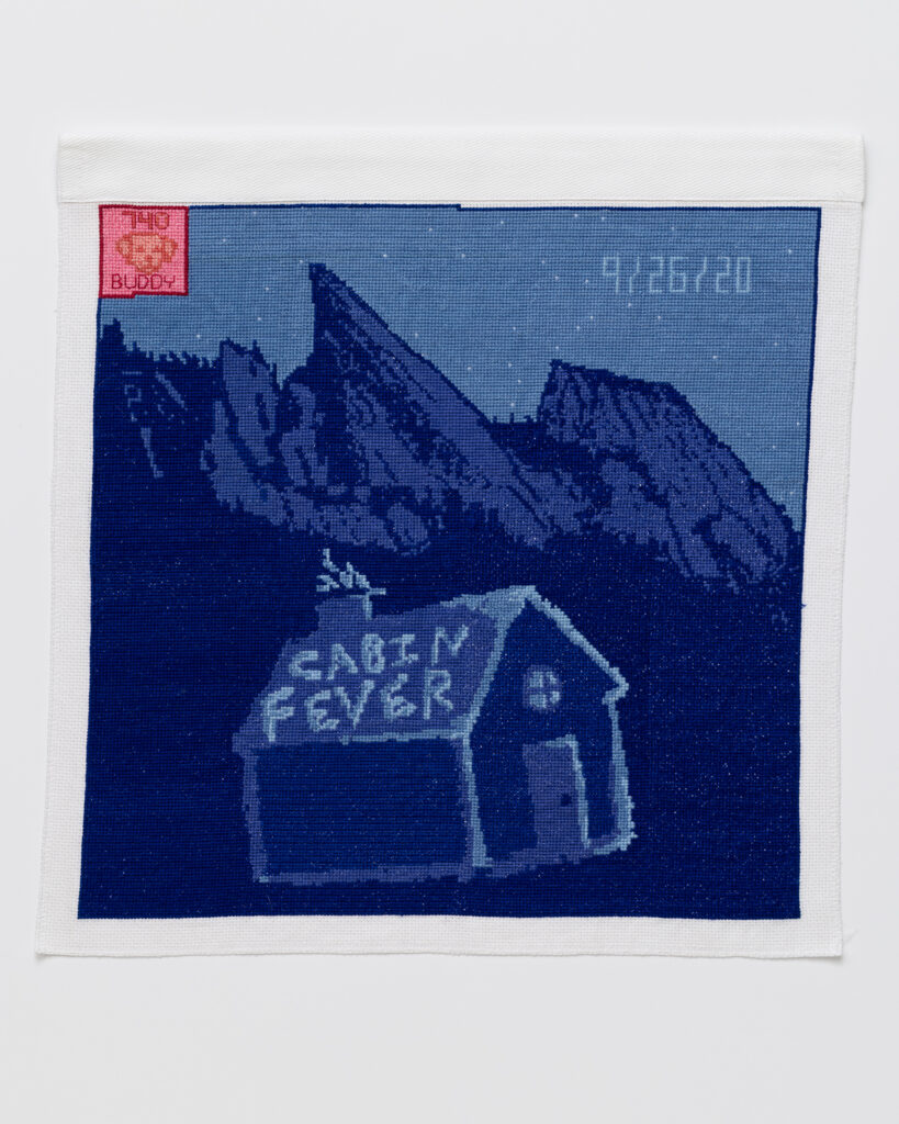 Cross stitch embroidery of small cabin at night in front of mountains. 