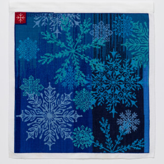 Cross stitch embroidery with turquoise and light blue snow flakes on a medium and dark blue background. A small red square is in the top left corner with a small pink snowflake inside.