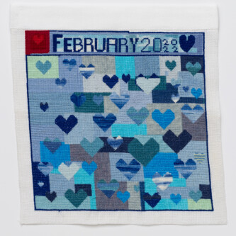 Cross stitch embroidery with various colored blue hearts on a background of vlue rectangles. "February 20 2022" is written across the top. There is a dark red square with a lighter red heart in the top left corner.