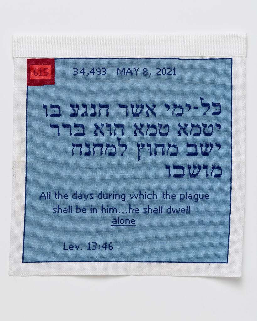 Cross stitch embroidery of Hebrew text written in dark blue thread on light blue background. At the top 